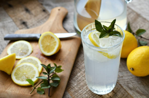 Lemons on a cutting board next to a glass of lemonade