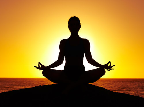 Silhouette of person meditating in front of sunrise