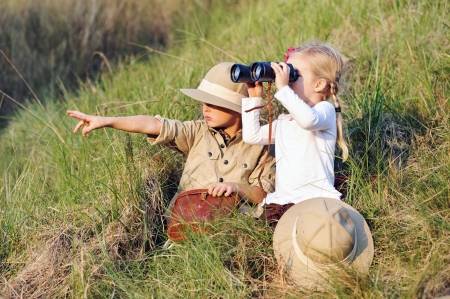 Young boy in safari gear pointing and a young girl looking through binoculars