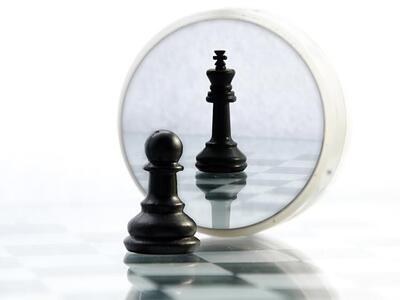 Pawn chess piece looking in a round mirror and seeing itself as the king