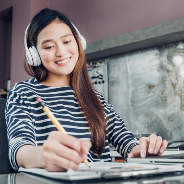 Young lady smiling, wearing headphones, and writing with a pencil